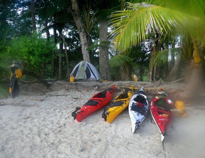 kayaks beached on white sand in front of tent in the woods